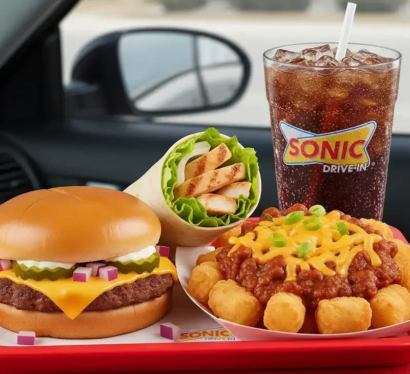 Sonic Drive-In meal with burger, chicken wrap, chili tots, and a cold drink served on a tray